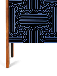 A modern sideboard or credenza with a black top and front featuring a blue and black geometric maze-like line pattern, supported by a light wood frame and single leg, shown against a plain white background.
