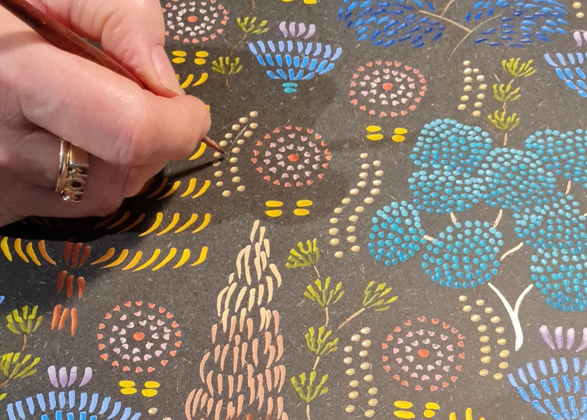 Hand holding a paintbrush painting details on a carved and painted  colourful floral design.