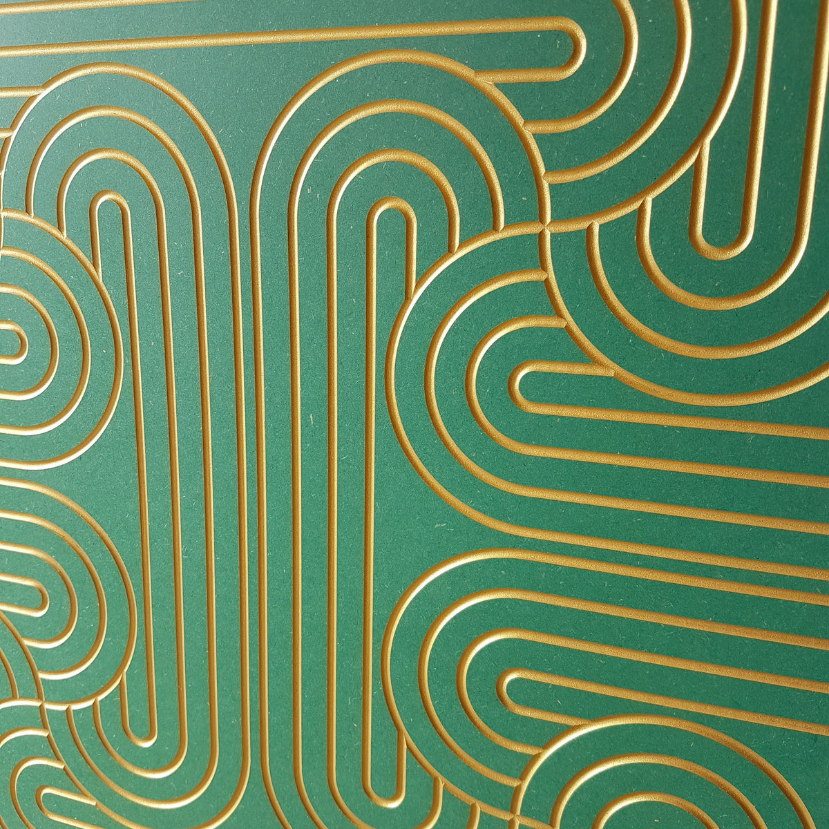 A close-up of a green panel or tile featuring a raised geometric pattern of interlocking gold lines.