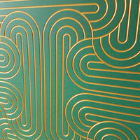A close-up of a green panel or tile featuring a raised geometric pattern of interlocking gold lines.