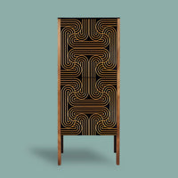 A tall, narrow cabinet or storage unit with a black front featuring a geometric gold line pattern, framed by warm brown wood sides and supported by slim legs, set against a solid muted teal background.
