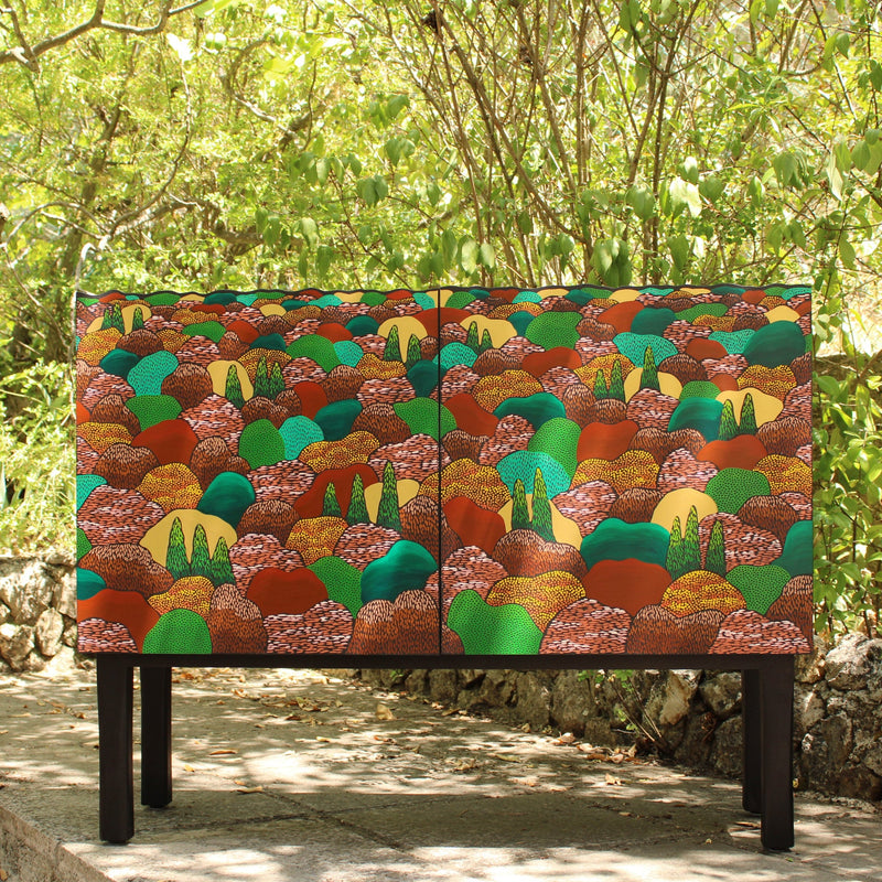 Colorful patterned cabinet in a natural setting with greenery and stone wall.