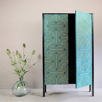 A Long door cabinet with handpainted loop pattern in gold on blue doors, with sides stained in black and a hard wax oil finish. 