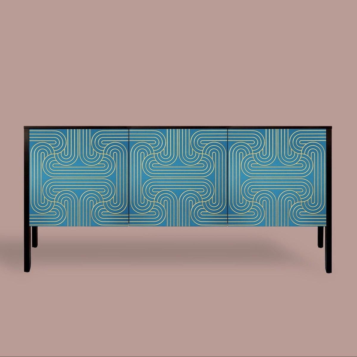 A modern three-door sideboard or credenza with a blue and gold geometric maze-like pattern on the doors, supported by slim black legs, set against a solid taupe background.