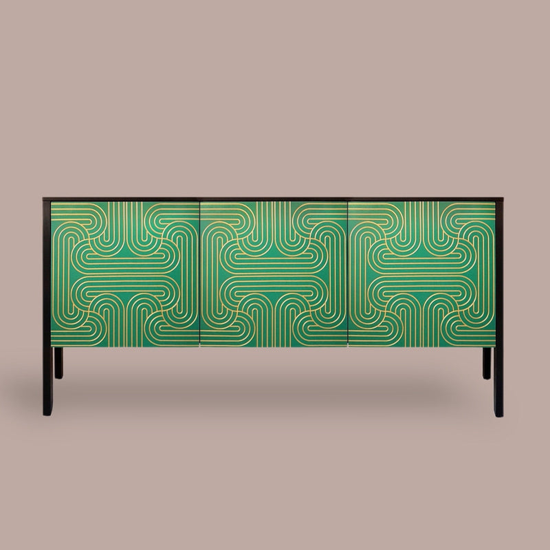 A modern sideboard or credenza with a green and gold geometric patterned front, supported by slim black legs, set against a solid taupe background.