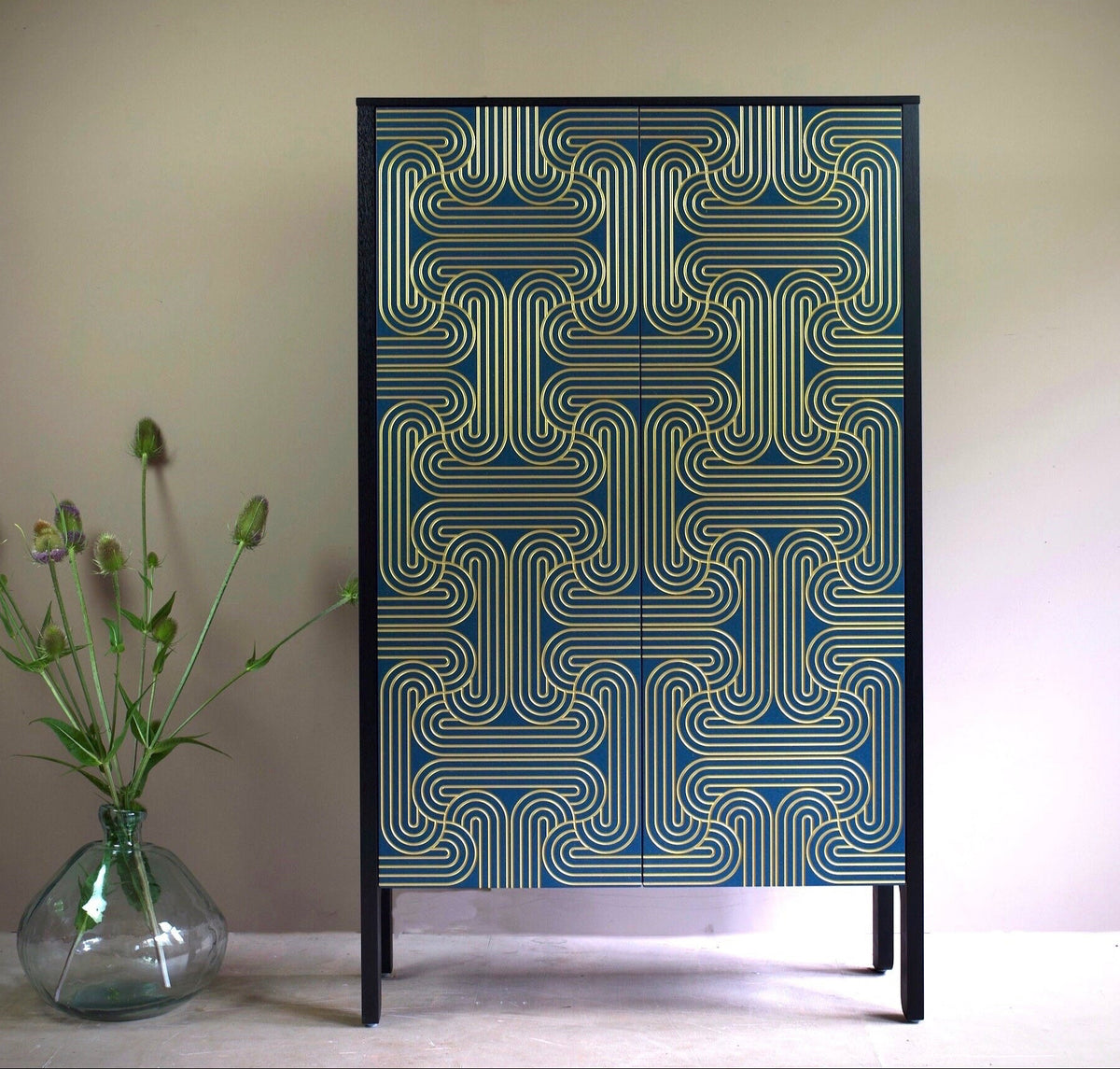 A cabinet with long doors featuring a geometric loop pattern in gold on blue doors and black sides
