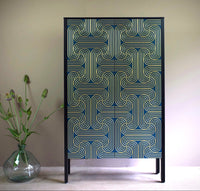 A cabinet with long doors featuring a geometric loop pattern in gold on blue doors and black sides